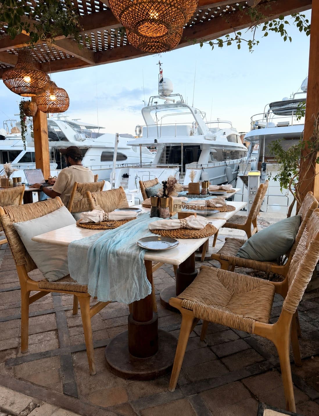 A laid table on the terrace with yachts moored behind it