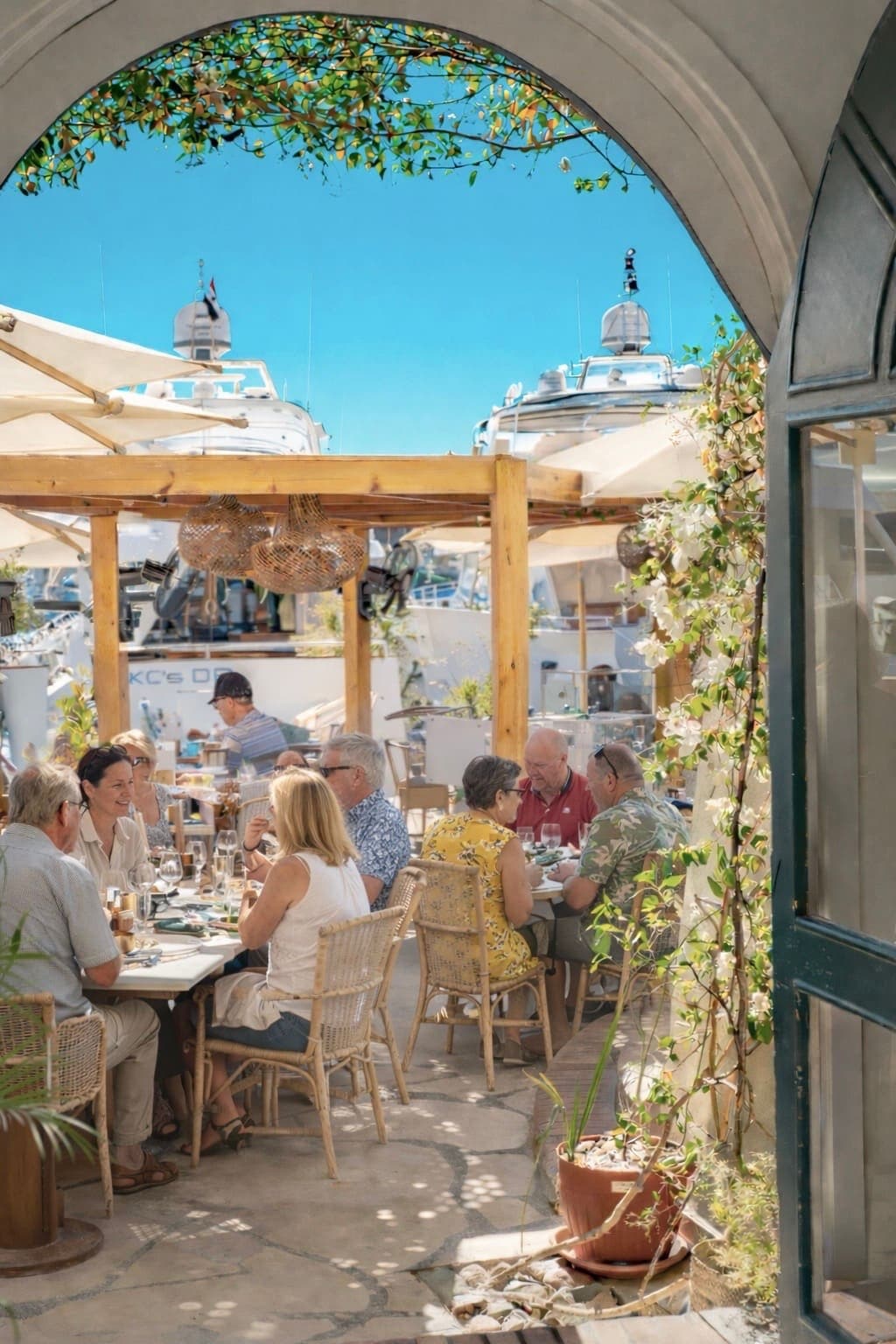 Guests under the pergola, greenery and boats in the background