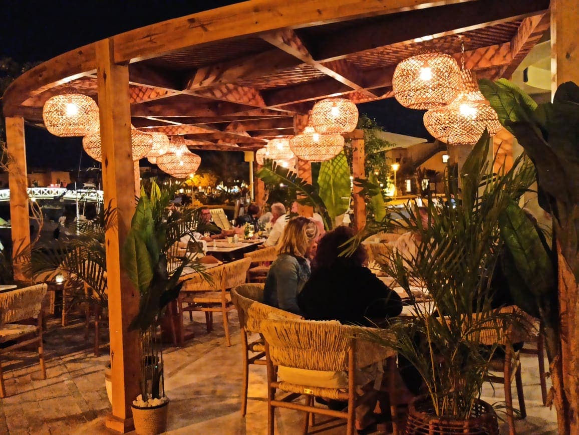 Evening under the pergola at Boho Café: rattan lamps lit, palms, guests at the tables