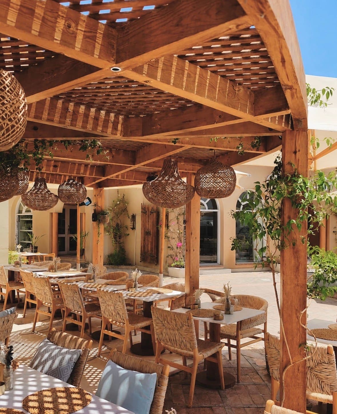 Pergola slats and rattan lamps above empty tables
