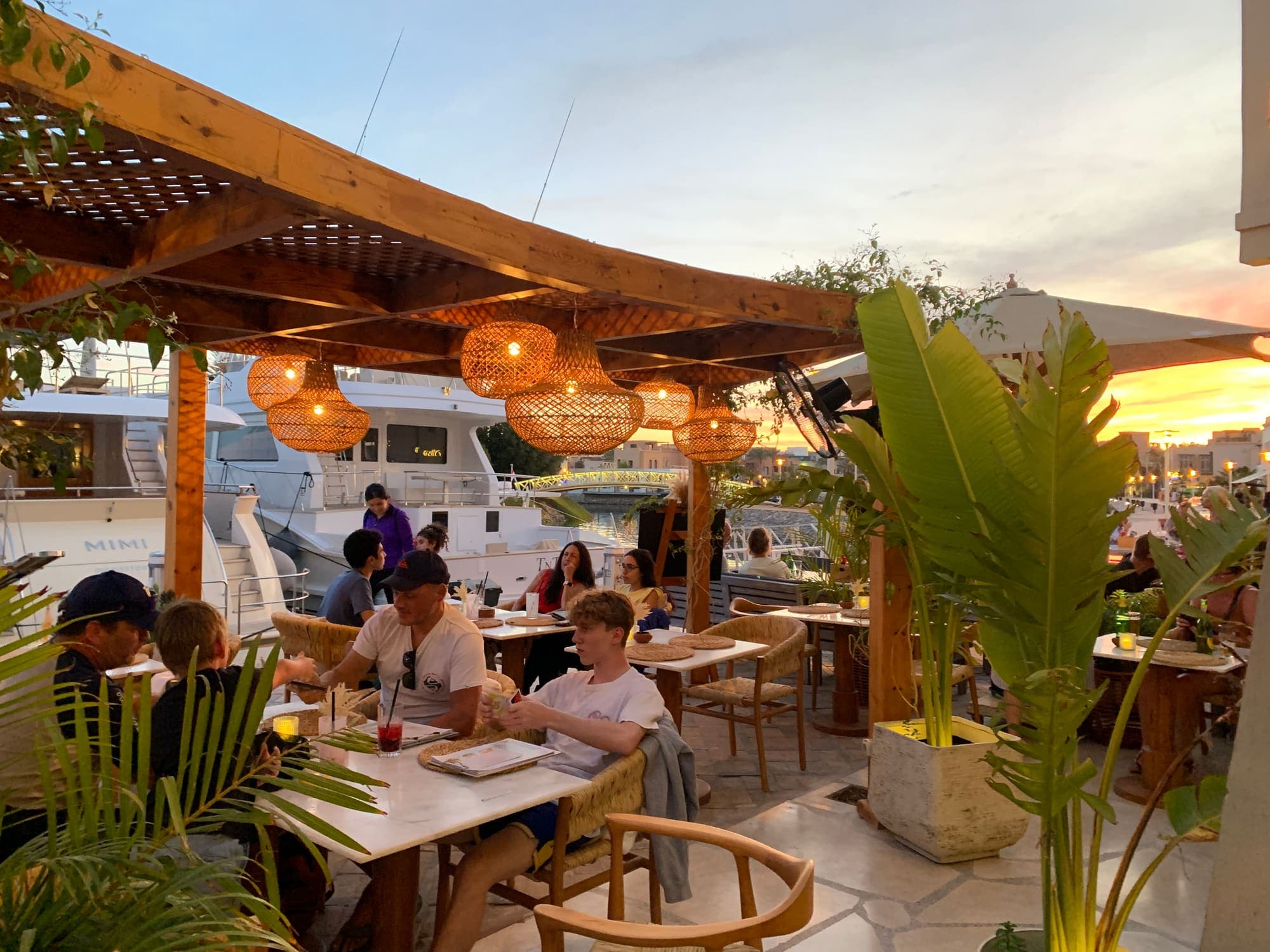 Families at the tables in the evening, lamps lit over the marina
